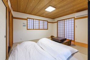 Ein traditioneller japanischer Raum mit Tatami-Boden, niedriger Holzbalkendecke, verschiebbaren Shoji-Türen und einem Bett mit weißer Bettwäsche.