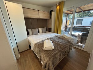 Ein Schlafzimmer mit Bett, Kopfstütze, einem Fenster mit Vorhängen und Blick nach draußen.