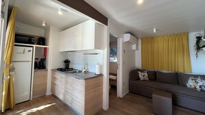 A compact kitchen with a refrigerator, microwave, and stove, a sofa, and a window with curtains.