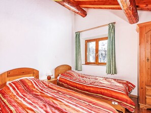 Een kamer met twee houten bedden, een raam met gordijnen en een houten garderobe.