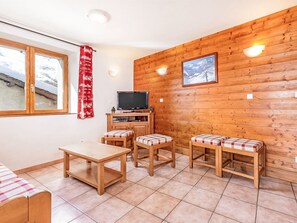 A room with a wooden wall, a television, a table, and two benches. - Balcon Cime de Caron by Interhome (Les Granges)
