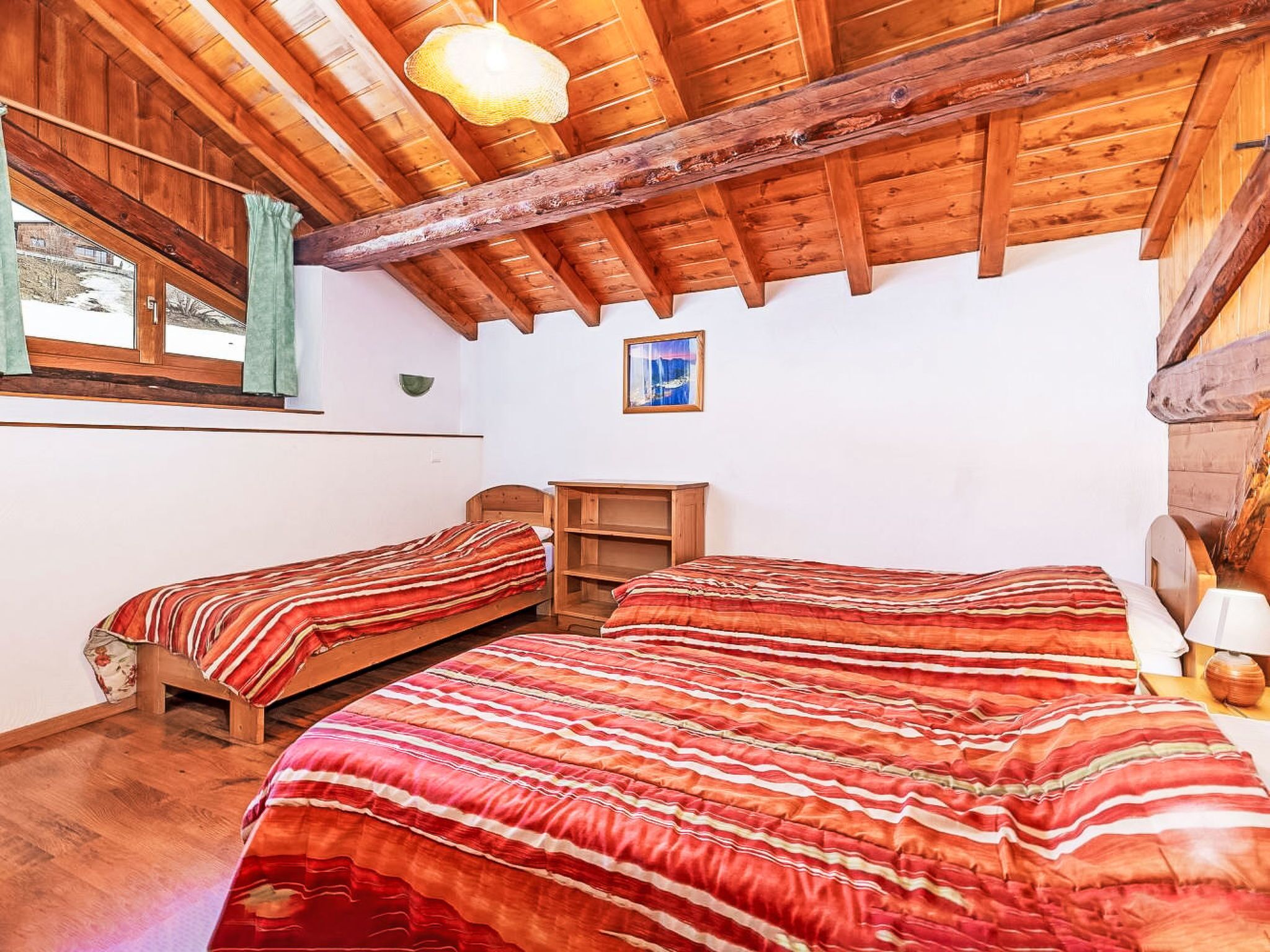 A room with two wooden beds, a wooden desk, a hanging light fixture, and a window with curtains.