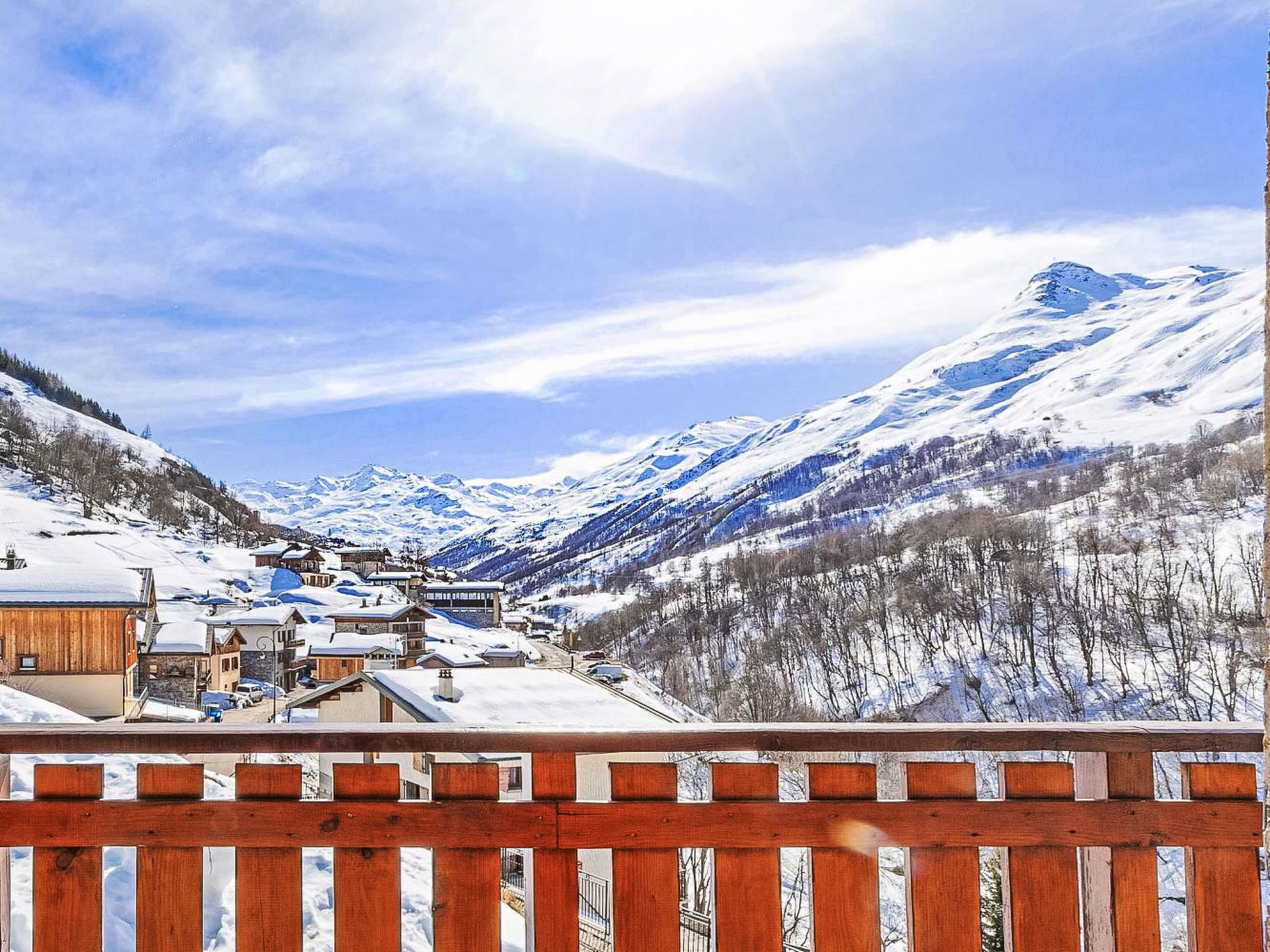 A snow-covered mountain village with wooden buildings and a wooden fence in the foreground.