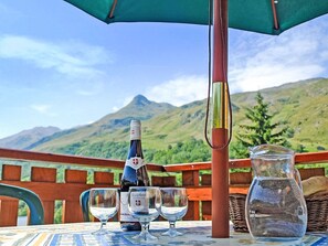 A table with a bottle of wine, three glasses, and a pitcher, set outdoors with a mountain view. - Balcon Cime de Caron by Interhome (Les Granges)