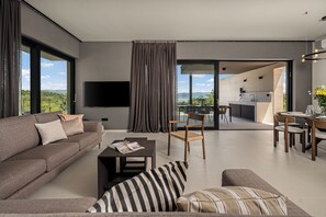 A modern living room with a sofa, a coffee table, and a TV. There is a dining area with a table and chairs. - Villa Serenis – a Modern New-Build with Private Pool and Breathtaking Sea Views (Labin)