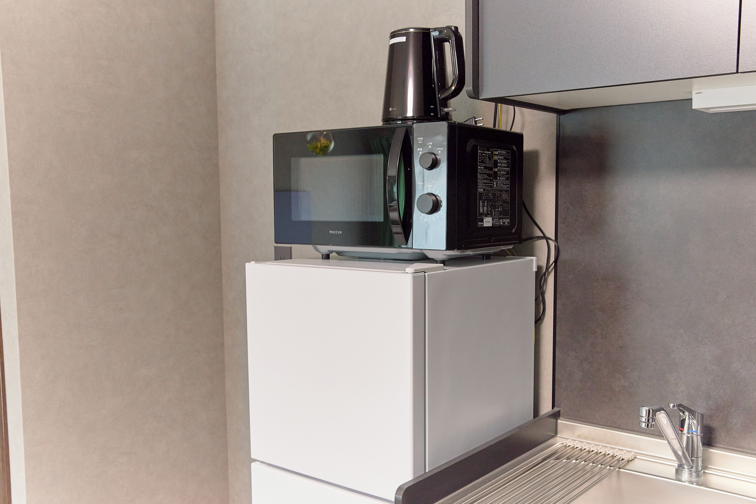 A compact kitchen with a microwave and coffee maker on a white refrigerator, a stainless steel sink, and a cabinet above.