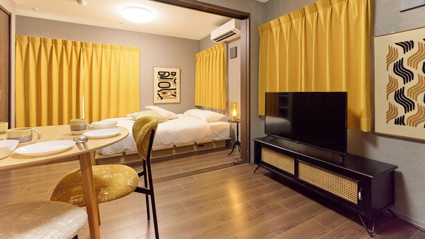 A hotel room with a bed, a TV, a dining table with chairs, and a mirror. - J-ARC Kamata (Ota-ku)