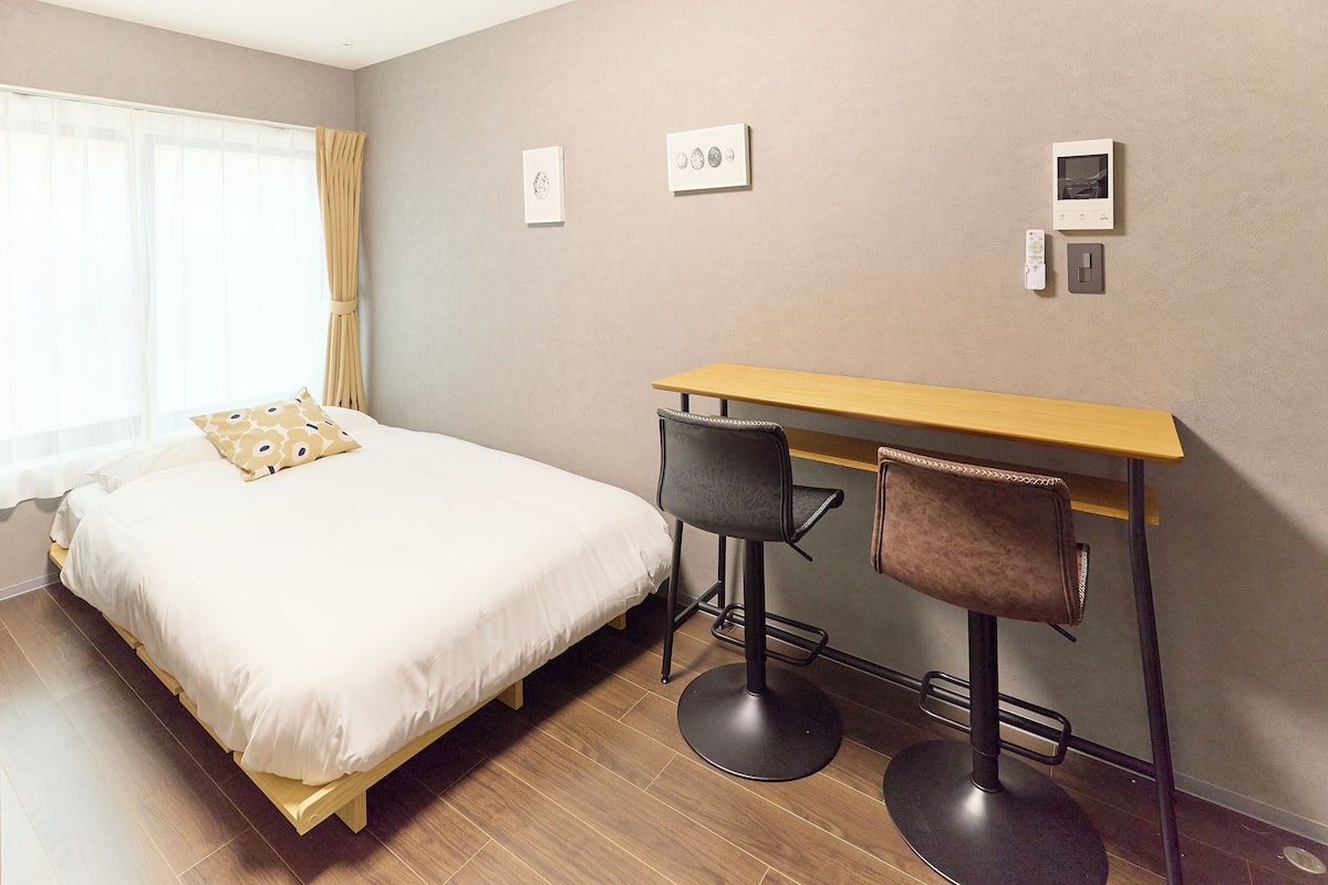 Une chambre à coucher avec un lit, un bureau, deux chaises et une fenêtre avec des rideaux.