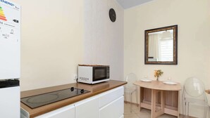 Una kitchenette con microondas, una mesita con sillas, un espejo y un reloj en la pared.