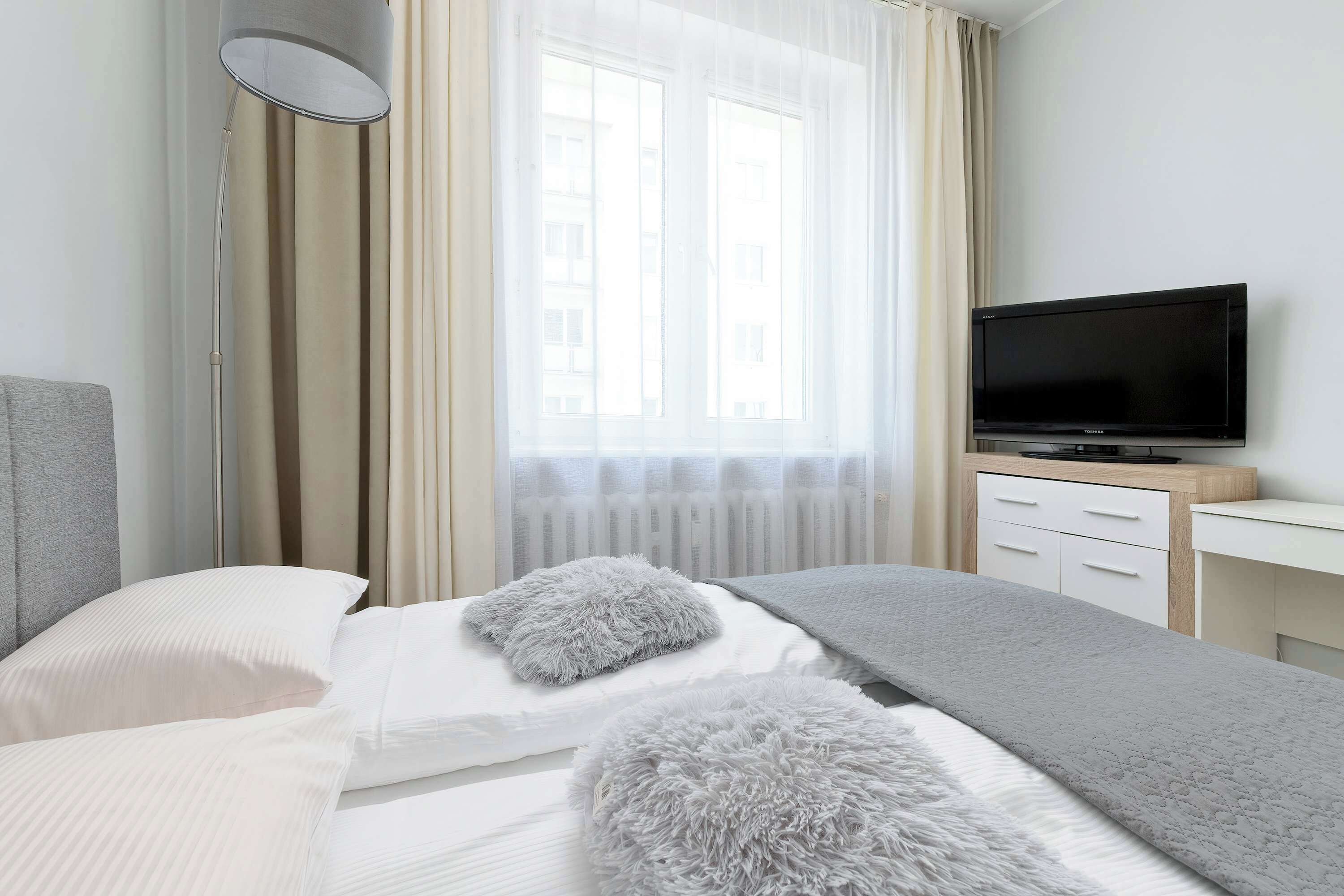 A hotel room with a bed, a television, a desk, and a window with curtains.