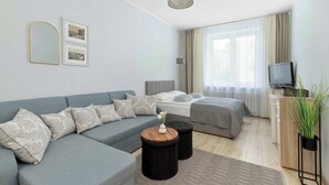 Un dormitorio moderno con un sofá gris, una cama, un televisor y una planta.