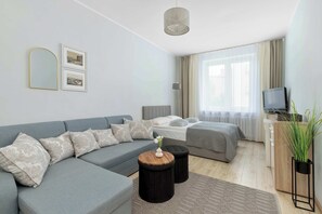 Ein modernes Schlafzimmer mit grauem Sofa, einem Bett, einem Fernseher und einer Pflanze.