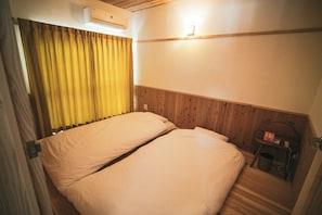 Ein Zimmer mit zwei Betten, einem hölzernen Kopfstück, einer Wand-Klimaanlage und einem kleinen Tisch mit Stuhl.