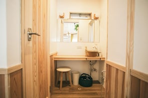 Ein schmaler Flur führt zu einem Badezimmer mit einem Holzkosmetikschrank, einem Waschbecken, einem Spiegel und einer Toilette.