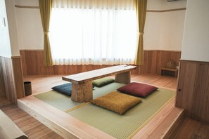 Ein Zimmer mit Tatami-Bodenbelag, einem niedrigen Holztisch und Kissen.