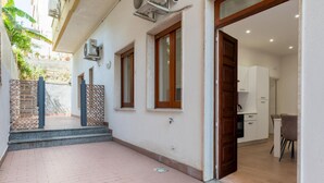 Un immeuble résidentiel doté d’une cour dallée, d’une porte en bois donnant sur une cuisine et d’un petit espace extérieur aménagé pour s’asseoir.