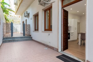 A residential building with a paved courtyard, a wooden door leading to a kitchen, and a small outdoor seating area. - GuestHost - Casa degli Oleandri (Naxos)