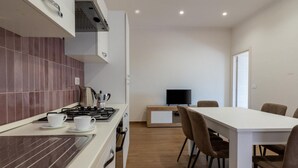 Une cuisine moderne avec une cuisinière, deux tasses blanches et un téléviseur en arrière-plan.