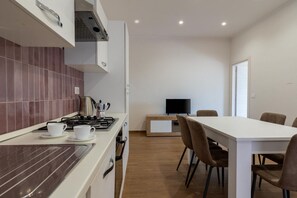 A modern kitchen with a stove, two white cups, and a television in the background. - GuestHost - Casa degli Oleandri (Naxos)