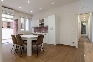A modern kitchen with white cabinets, a dining table with chairs, and a visible air conditioning unit. - GuestHost - Casa degli Oleandri (Naxos)
