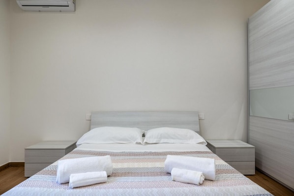 A clean, modern hotel room with a bed, two bedside tables, and a wall-mounted air conditioner. - GuestHost - Casa degli Oleandri (Naxos)