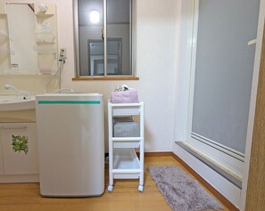 A bathroom with a white washing machine, a white shelf with towels, a wooden floor, and a window.