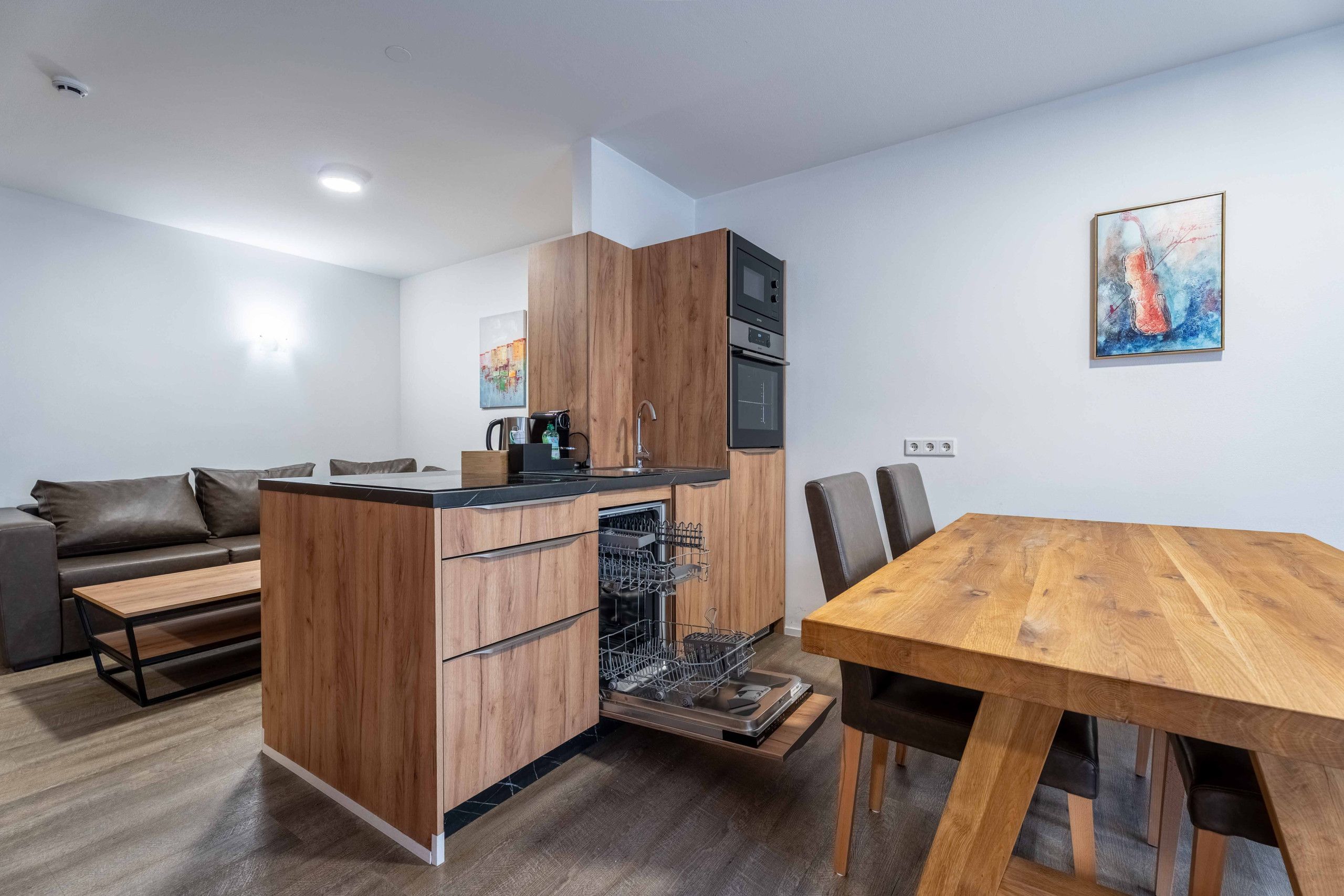 Une cuisine compacte dotée d’appareils électroménagers intégrés, un coin repas avec une table en bois et un canapé dans l’espace de vie.