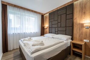 Una habitación de hotel moderna con una cama grande, cabecera de madera, lámparas de noche y una mesita de noche de madera.