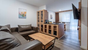 En moderne stue med sofa, sofabord, træskab og et køkkenområde med spisebord.