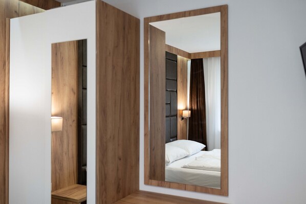 A modern bedroom with a large mirror, wooden paneling, a bed with white linens, and a nightstand with a lamp. - Maiskogelblick Apartments - TOP 4, Garden & Sauna (Piesendorf)