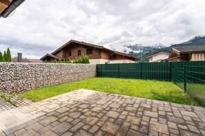 A courtyard with a paved area, stone wall, and green fence. - Maiskogelblick Apartments - TOP 2, Garden & Sauna (Piesendorf)