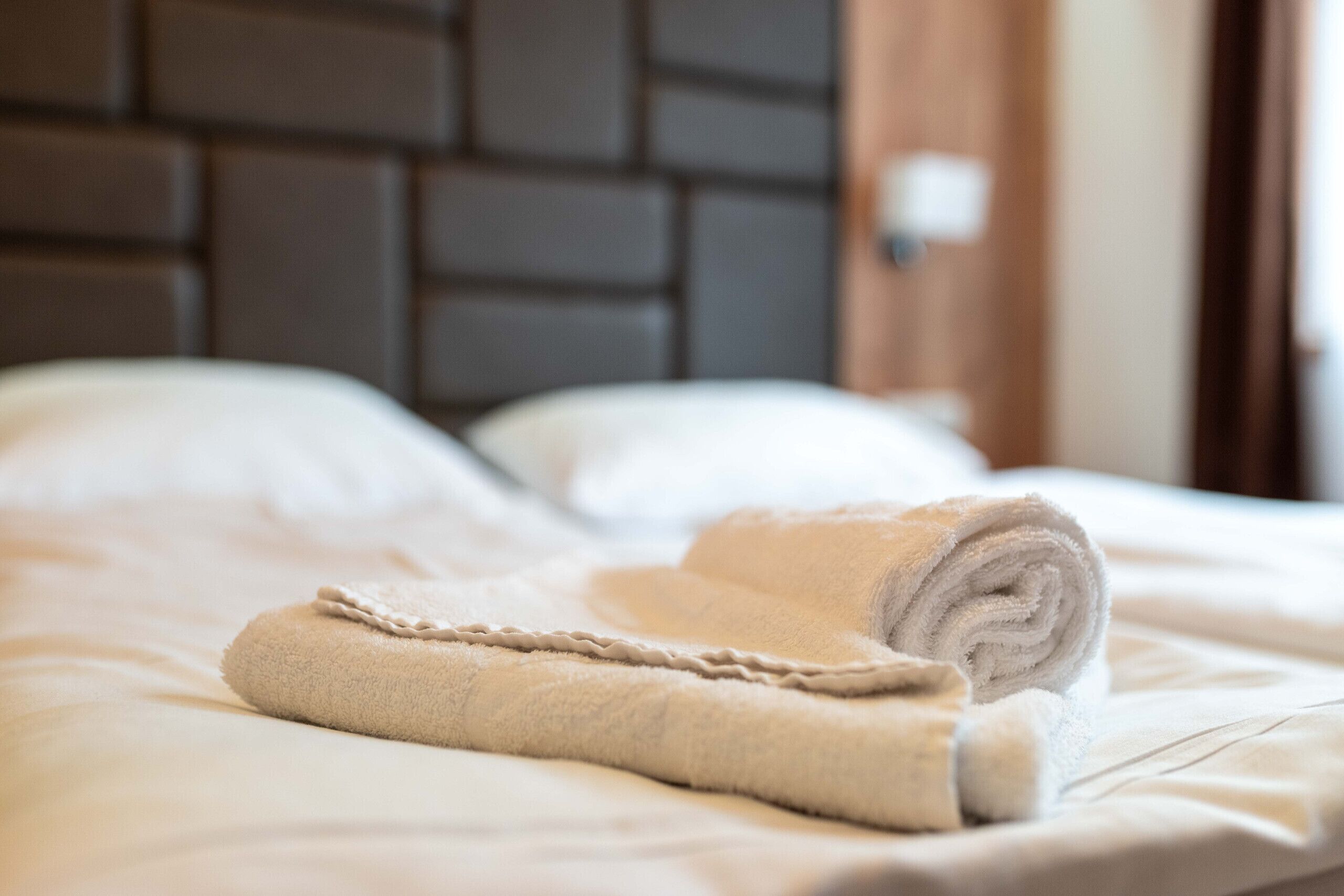A neatly made bed with a rolled towel and a pillow.