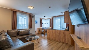 A modern living room with a sofa, coffee table, and a dining area with a wooden table and chairs. - Maiskogelblick Apartments - TOP 9, Balcony & Sauna (Piesendorf)