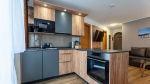 A modern kitchen with wooden cabinets, a microwave, a stove, and a sink. - Maiskogelblick Apartments - TOP 9, Balcony & Sauna (Piesendorf)