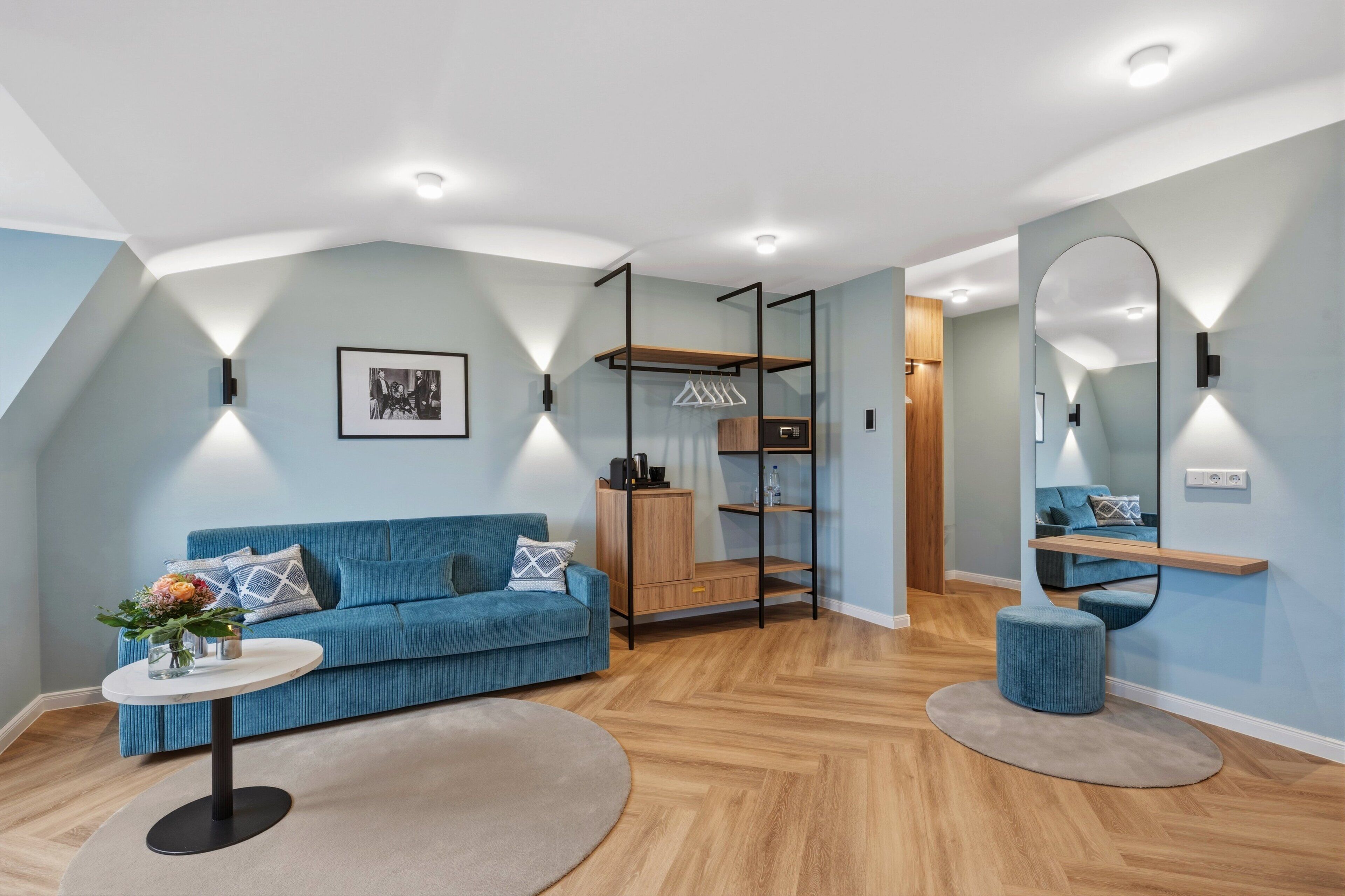 Una sala de estar moderna con un sofá azul, una mesa de centro redonda, un mueble de madera y un espejo en la pared.