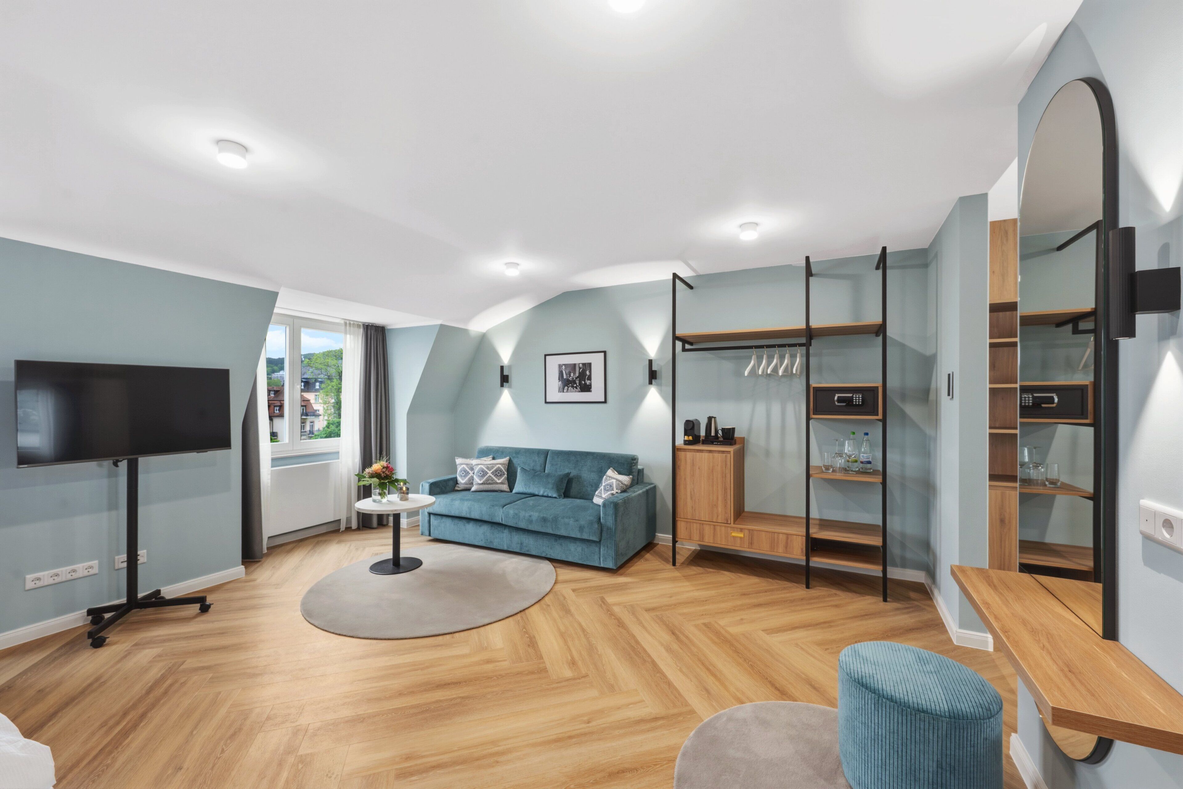 Un salon moderne avec un téléviseur à écran plat, un canapé bleu, une table basse ronde et un meuble en bois.