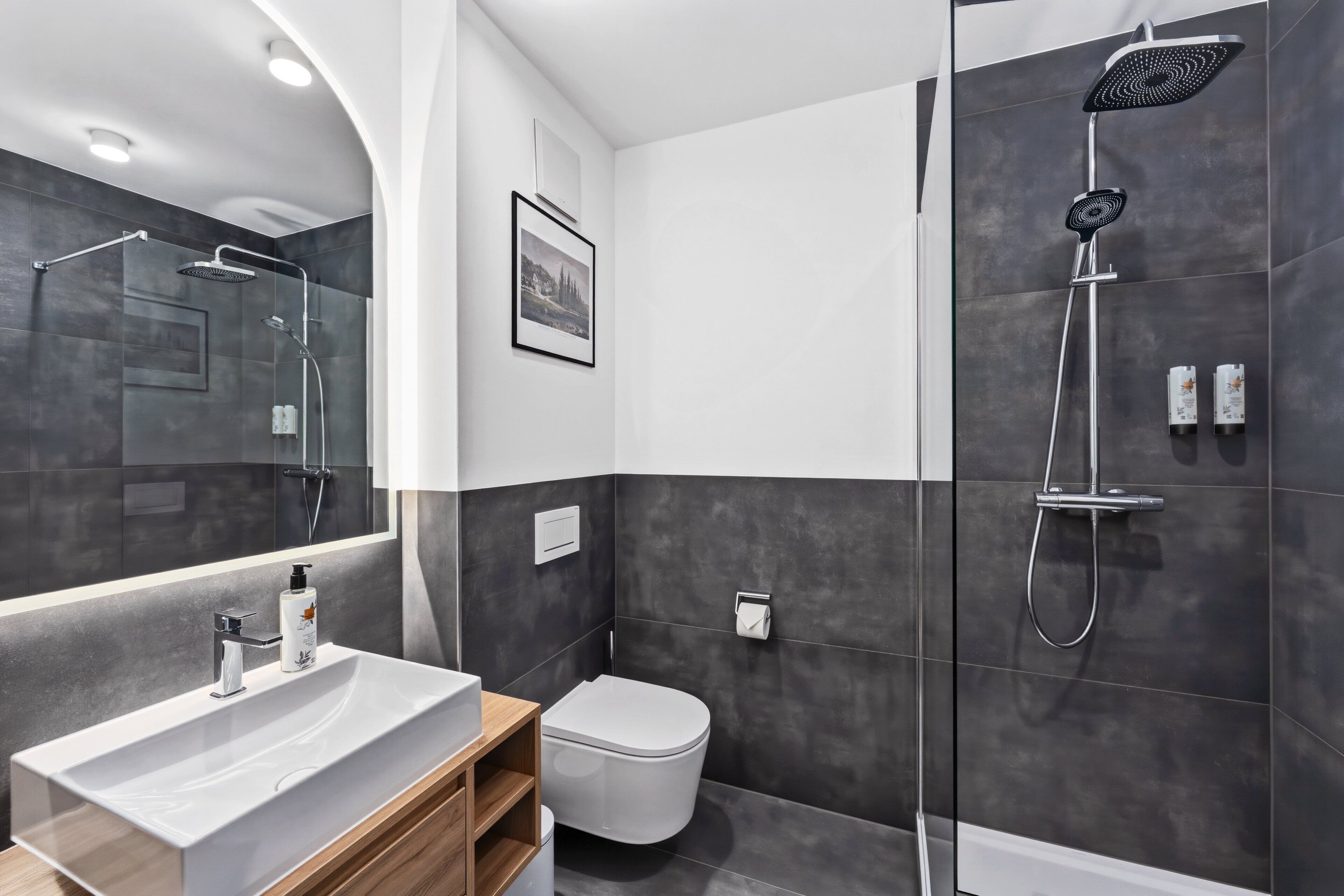Une salle de bain moderne avec un grand miroir, un lavabo blanc, des toilettes et un espace douche.