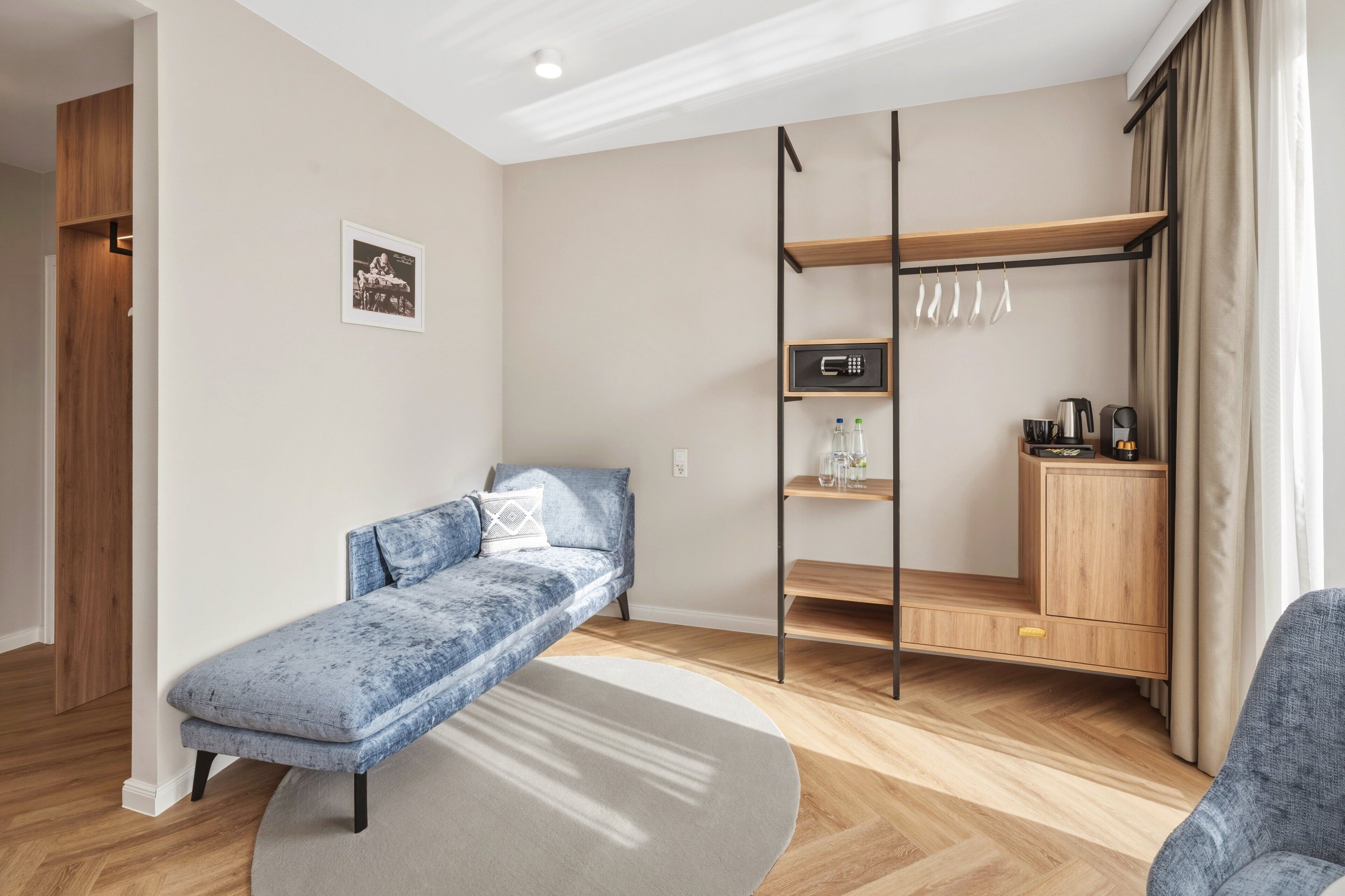 Una habitación moderna con un sofá, una cama pequeña, un armario de madera y una estantería con objetos.