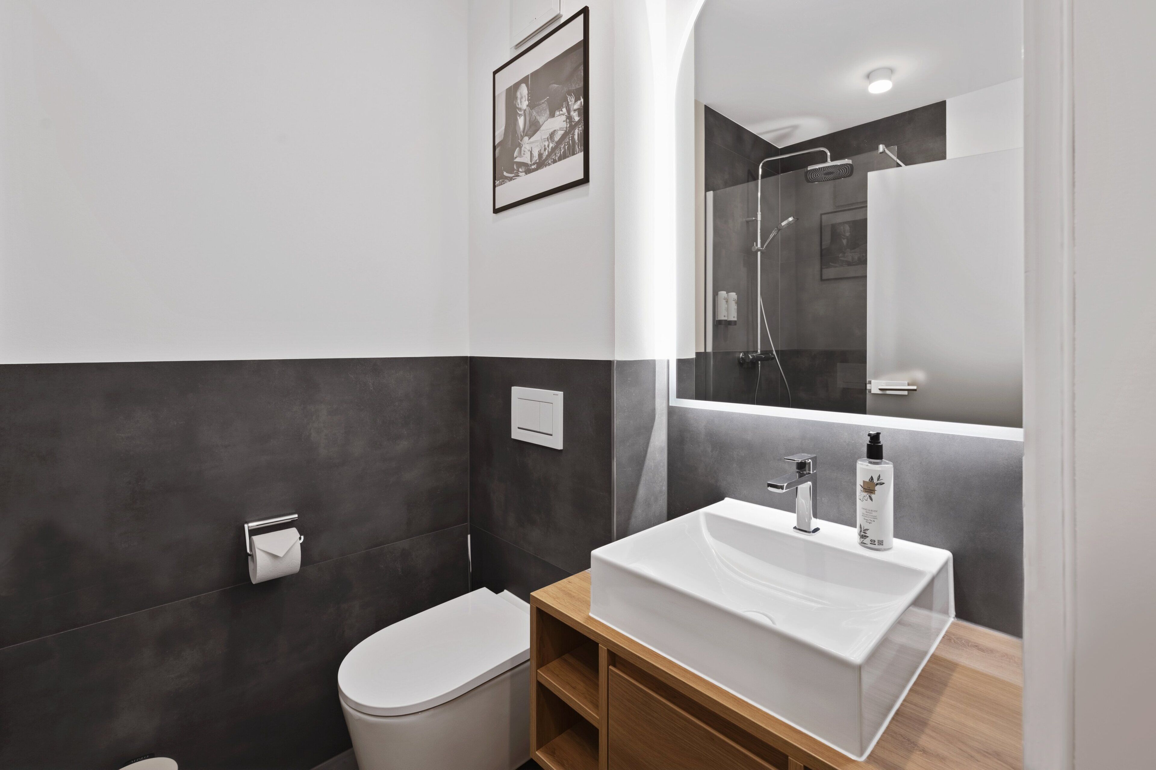 Un baño moderno con un lavabo blanco, azulejos oscuros en la pared, un inodoro y una ducha.