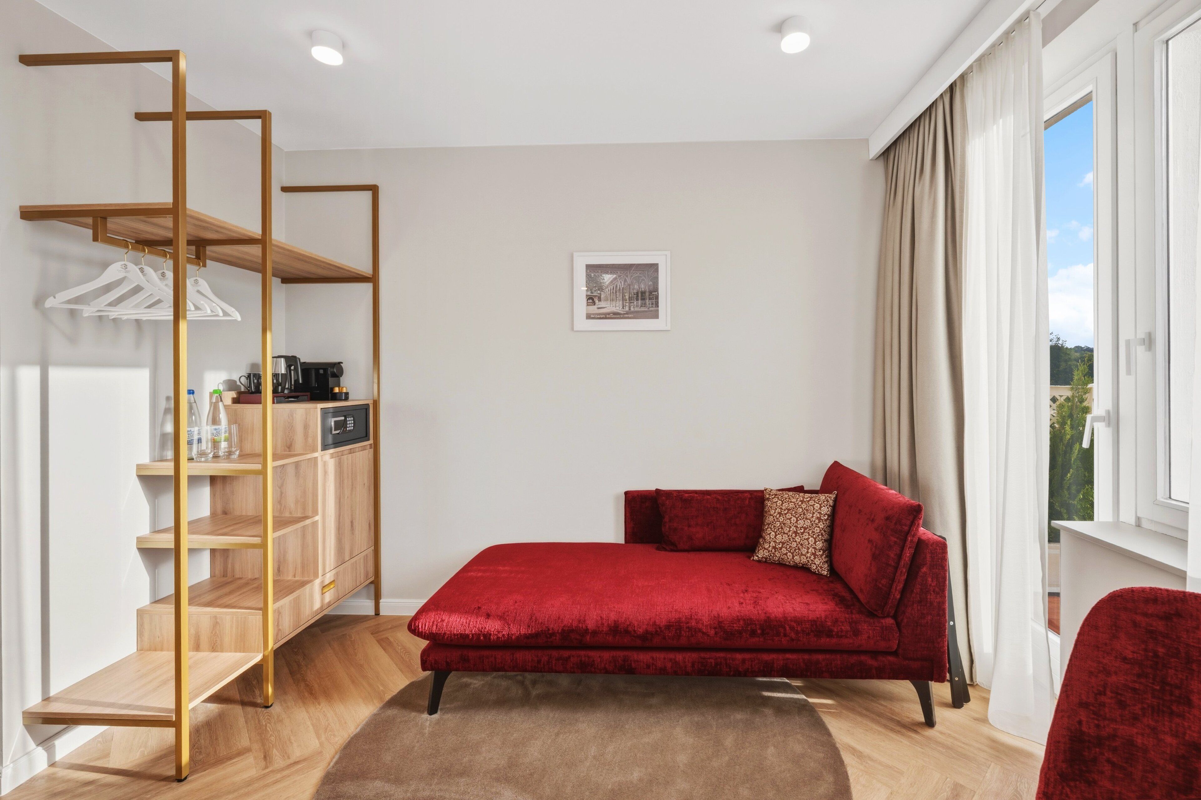 A modern room with a red sofa, a wooden shelf unit, and a window with curtains.
