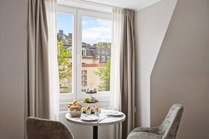 Una habitación con una mesa de comedor lista para dos personas, una ventana con cortinas y vistas a edificios.