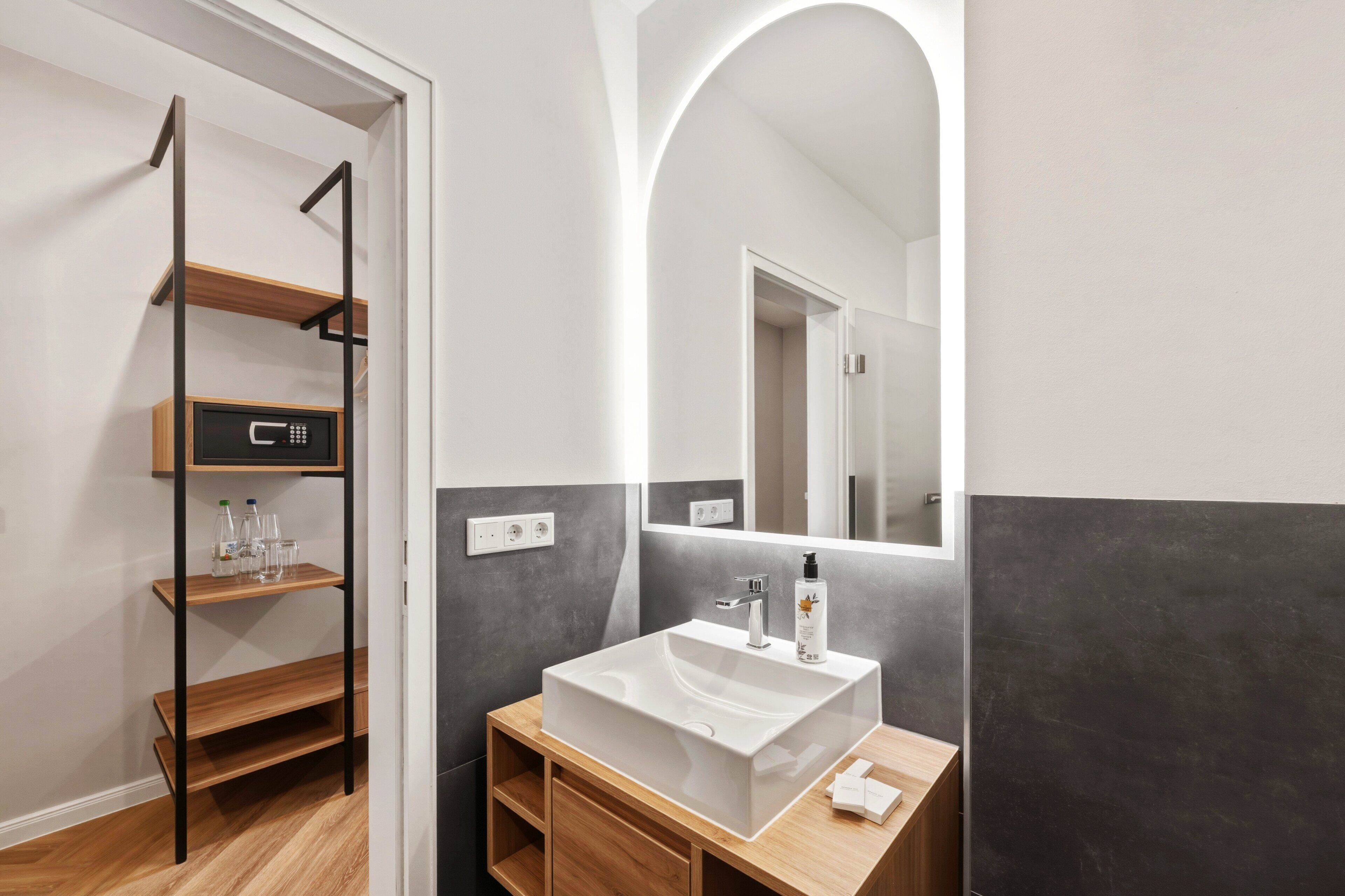 A modern bathroom with a white sink, wooden shelves, and a mirror.