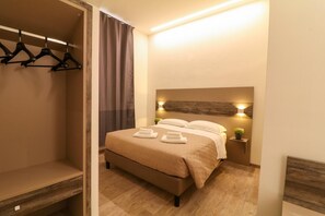 A hotel room with a bed, a bedside table with a lamp, a hanging coat rack, and a window with curtains. - Superior Room rom 1 to 2 person near San Pietro (Roma)