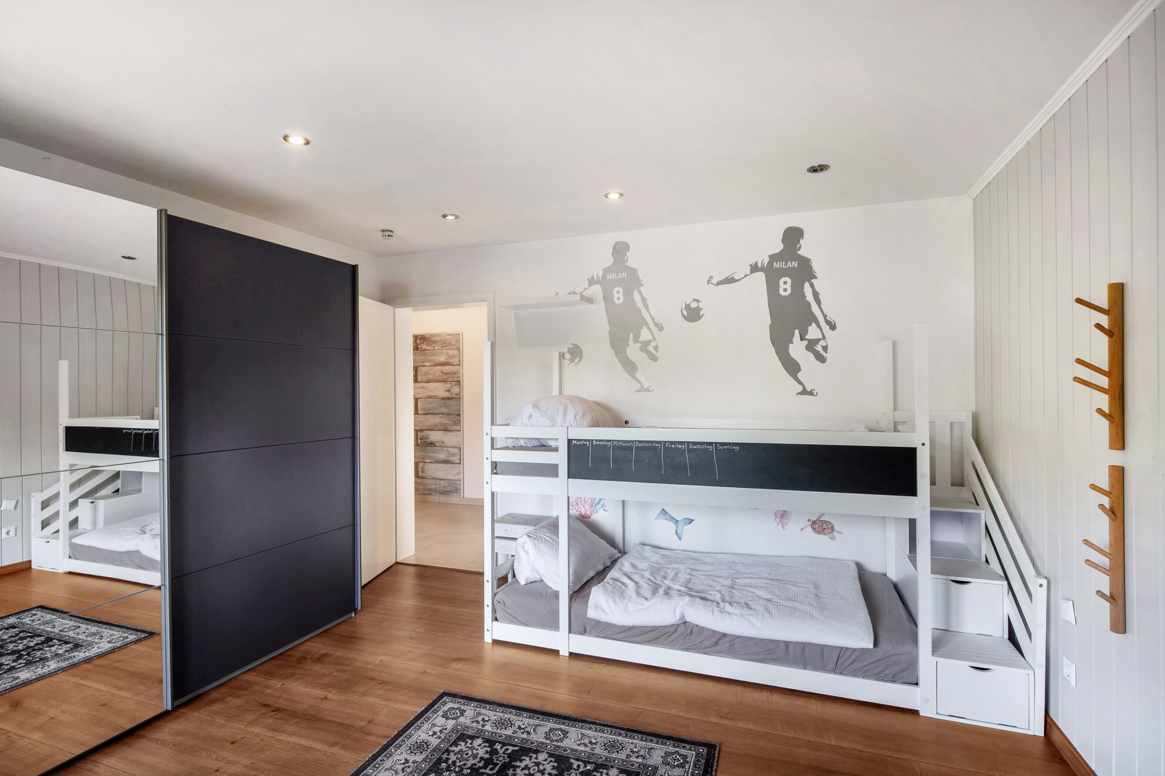A bedroom with a bunk bed, a wardrobe, a basketball-themed wall, and a patterned rug.
