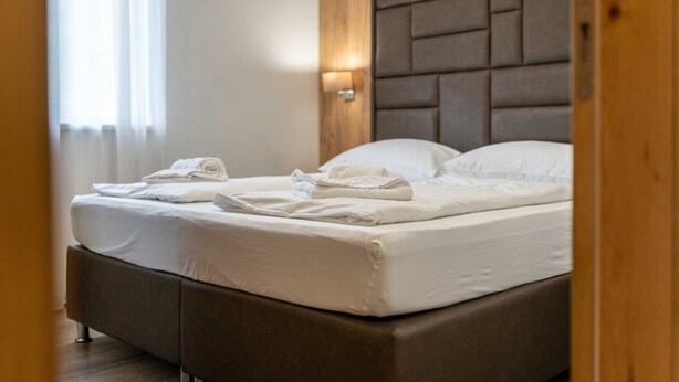 Een netjes opgemaakt bed met witte lakens en handdoeken, een houten hoofdbord en een wandlamp.