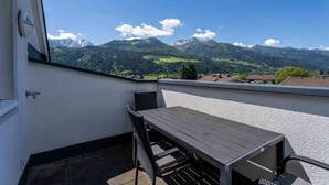 Un balcon avec une table et des chaises en bois, une vue sur les montagnes et un ciel dégagé.