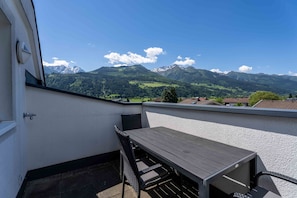 Ein Balkon mit Holztisch und Stühlen, Blick auf Berge und einen klaren Himmel.