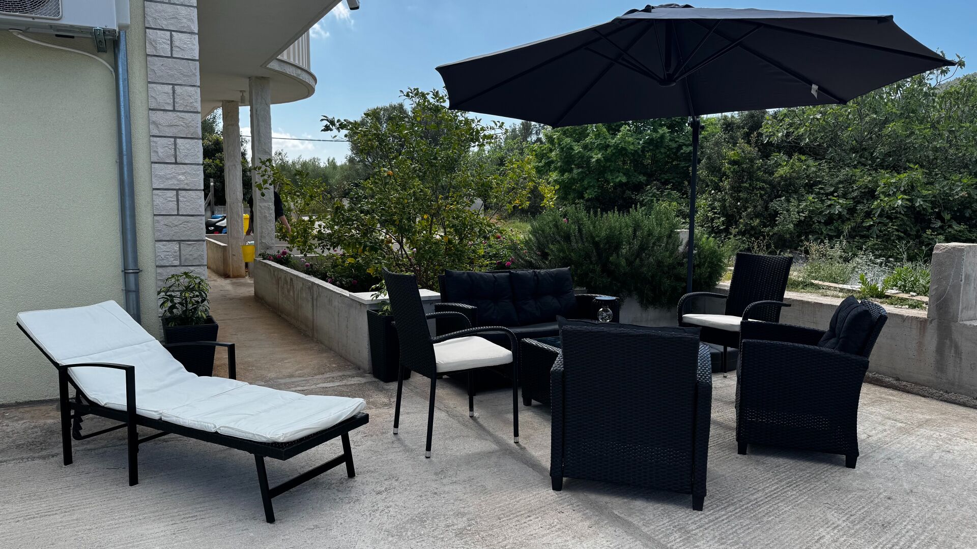 Une terrasse extérieure avec un fauteuil de relaxation, une table à manger, des chaises et un parasol.