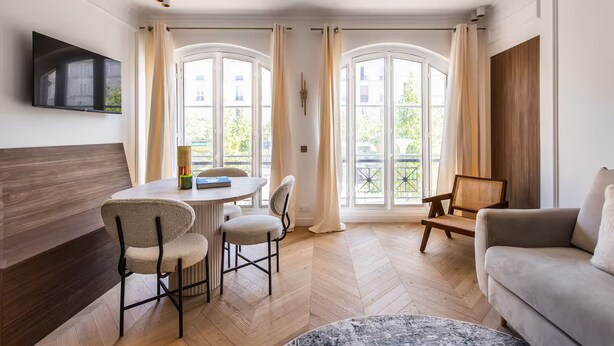 Een moderne woonkamer met een bank, een eettafel met stoelen en een aan de muur bevestigde televisie.
