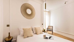 Een keurig opgemaakt slaapkamer met een bed, kussens, een ronde spiegel, een stoel en een nachtkastje.